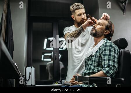 Attenzione barbiere in piedi vicino al cliente e con rasoio Foto Stock