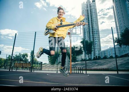 Espressivo giovane donna tenendo la sua chitarra e jumping Foto Stock