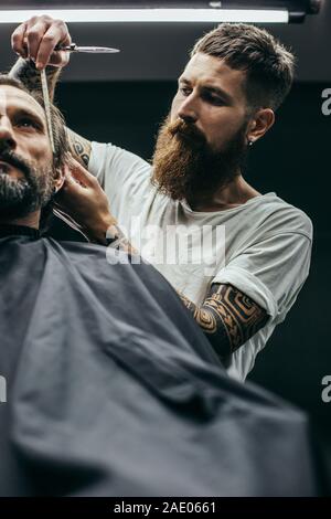 Barbuto barbiere in piedi vicino all'uomo sorridente e il suo taglio di capelli Foto Stock