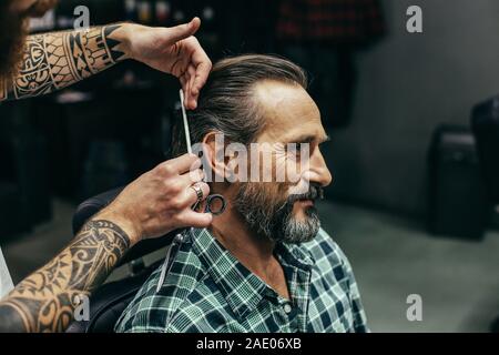 Allegro uomo sorridente mentre il barbiere il suo taglio di capelli Foto Stock