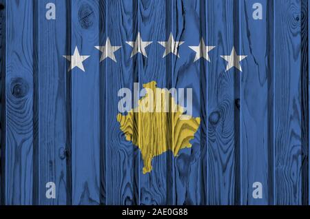 Bandiera del Kosovo raffigurato in luminosi colori di vernice sul vecchio muro di legno vicino. Textured banner su sfondo irregolare Foto Stock