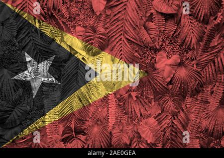 Timor Leste bandiera raffigurata su molti fogli di monstera palme. Alla moda sullo sfondo Foto Stock