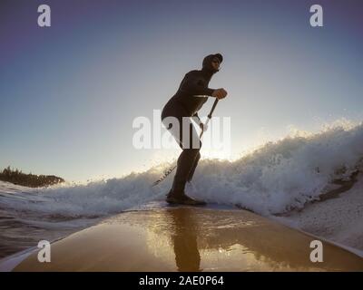 Uomo avventuroso Surfer su un dispositivo di compressione scheda è navigare nell'oceano durante una mattina di sole nella stagione autunnale. Prese a Long Beach, Tofino, Isola di Vancouver, Foto Stock