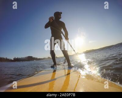 Uomo avventuroso Surfer su un dispositivo di compressione scheda è navigare nell'oceano durante una mattina di sole nella stagione autunnale. Prese a Long Beach, Tofino, Isola di Vancouver, Foto Stock