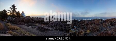 Bella vista panoramica del Rocky costa dell'Oceano Pacifico durante un colorato NUVOLOSO TRAMONTO con il faro in background. Prese su Wild Pacific Trail Foto Stock