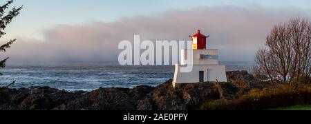 Bella vista panoramica del faro sul roccioso costa dell'Oceano Pacifico durante un colorato nuvoloso sunrise. Prese su Wild Pacific Trail in Ucluelet, Foto Stock