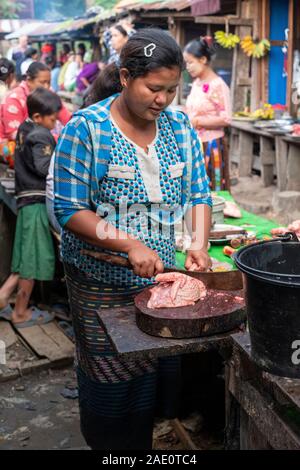 Una giovane donna birmana trita fino un pollo fresco per la vendita con un grande coltello da prosciutto in un villaggio marketplace nelle zone rurali del Myanmar (Birmania) Foto Stock