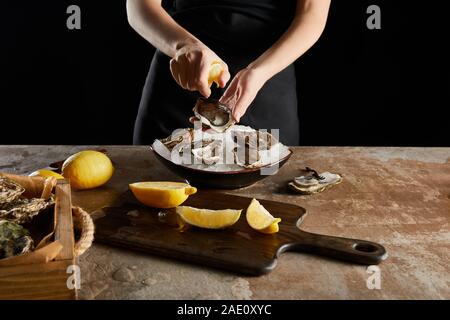 Vista ritagliata della donna la spremitura di limone su oyster isolato su nero Foto Stock