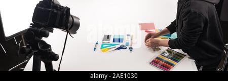 Vista ritagliata del fotografo femmina rendendo laici piatta con forniture per ufficio commerciale per il tiro di foto su bianco, scatto panoramico Foto Stock