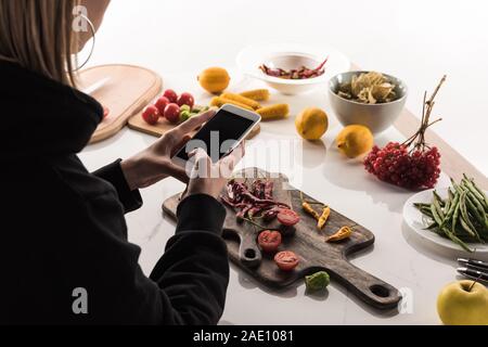 Vista ritagliata del fotografo rendendo la composizione degli alimenti per la fotografia commerciale sullo smartphone Foto Stock