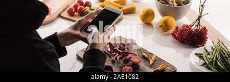 Vista ritagliata del fotografo rendendo la composizione degli alimenti per la fotografia commerciale sullo smartphone Foto Stock