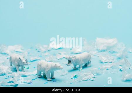 Giocattoli di bianco di ippopotamo, di rinoceronte e orso con immondizia di plastica su sfondo blu, benessere animale concetto Foto Stock