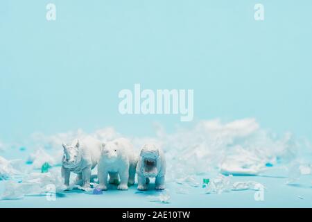 Giocattoli di bianco di ippopotamo, di rinoceronte e orso con immondizia di plastica su sfondo blu, benessere animale concetto Foto Stock