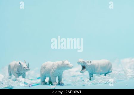 Giocattoli di bianco di ippopotamo, di rinoceronte e orso con immondizia di plastica su sfondo blu, benessere animale concetto Foto Stock