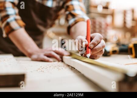 Vista ritagliata dell uomo con matita vicino a tavola in legno e nastro di misurazione Foto Stock