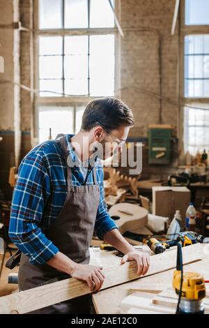 Vista laterale del barbuto falegname in grembiule azienda plank vicino a  sega circolare Foto stock - Alamy