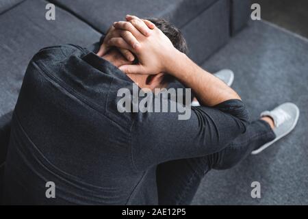 Elevato angolo di visione dell'uomo con il mal di testa di toccare la testa in appartamento Foto Stock