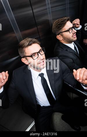 Angolo di alta vista di paura imprenditore della tuta con claustrofobia in ascensore Foto Stock