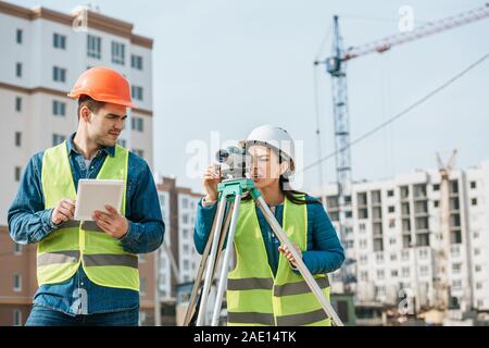 Periti che lavorano con tavoletta digitale e livello di misurazione sul sito in costruzione Foto Stock