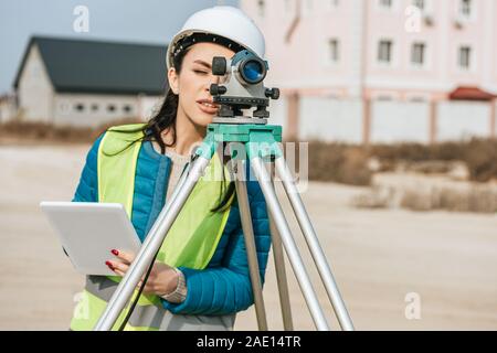Geometra femmina con tavoletta digitale guardando attraverso il livello di misurazione Foto Stock