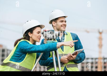 Geometra cerca attraverso il livello digitale e rivolto in direzione opposta al collega con la compressa Foto Stock