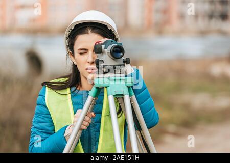 Attraente surveyor in hardhat lavora con livello digitale Foto Stock