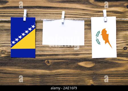 Appendere bandiere della Bosnia Erzegovina e Cipro attaccata alla corda con vestiti perni con copia spazio bianco sulla nota carta su sfondo di legno.Diplomatic Foto Stock