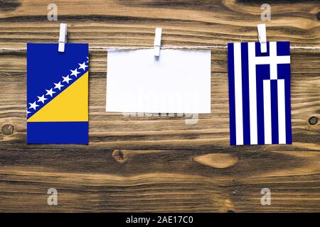 Appendere bandiere della Bosnia Erzegovina e Grecia attaccata alla corda con vestiti perni con copia spazio bianco sulla nota carta su sfondo di legno.Diplomatic Foto Stock