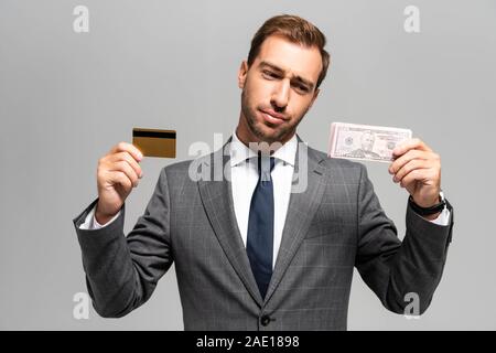 Bello e triste imprenditore nel soddisfare azienda Carte di credito e banconote di dollari isolato su grigio Foto Stock