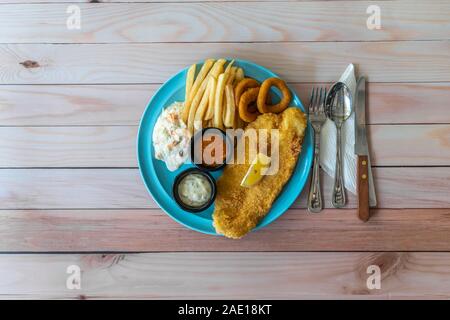 Fish & Chips con patatine fritte, coleslaw e anelli di cipolla, cibo occidentale sul concetto di tabella. Lay piatto vista dall'alto in basso. Foto Stock