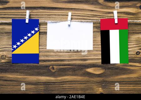 Appendere bandiere della Bosnia Erzegovina e Emirati Arabi Uniti attaccato alla corda con vestiti perni con copia spazio sulla nota di colore bianco su carta backgrou in legno Foto Stock