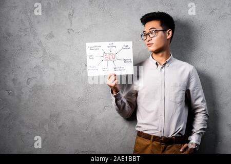 Asian seo manager di detenzione e guardando la carta con le parole il concetto di seo Foto Stock