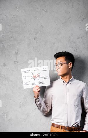 Asian seo manager di detenzione e guardando la carta con le parole il concetto di seo Foto Stock