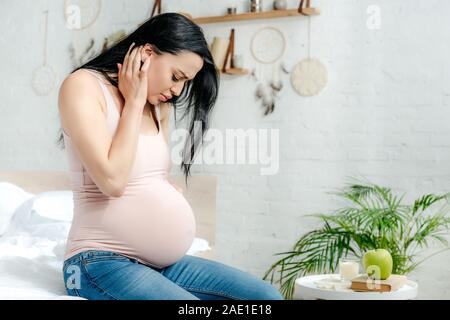 Preoccupato per la donna incinta avente il dolore e guardando a pancia in camera da letto Foto Stock