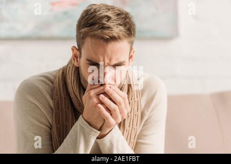 Uomo malato in caldi sciarpa tossire in mani piegate Foto Stock