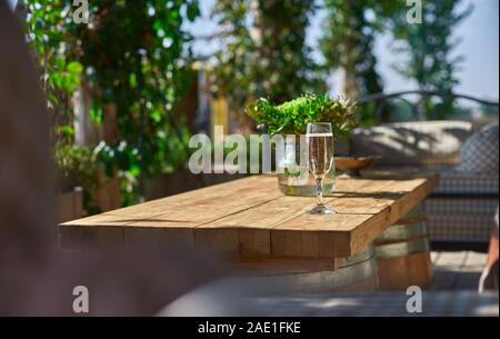 Accogliente terrazzo con divani per il riposo, il vetro con champagne su un tavolo di legno. Giornata di sole. Foto Stock