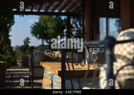 Accogliente terrazzo con divani per il riposo, il vetro con champagne su un tavolo di legno. Giornata di sole. Foto Stock
