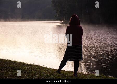 L'immagine dietro la donna in piedi sul prato e la nebbia galleggiare sull'acqua a Pang Tong serbatoio in Mae Hong Son , della Thailandia. Foto Stock