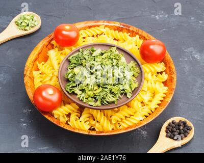 Pastina nel recipiente di legno, piccoli pomodori, il cipollotto, pepe nero su nero sfondo concreto. Mangiare sano concetto Foto Stock