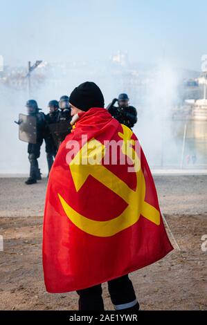 Dicembre 05, 2019, Lione, Auvergne-Rhône-Alpes, France-Demonstration contro la riforma del sistema pensionistico. Un dimostratore con una bandiera comunista sulla sua schiena in fr Foto Stock