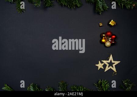 Addobbi natale (Natale baubles, stelle e poco presenta) su sfondo nero incorniciate da Abete rami Foto Stock