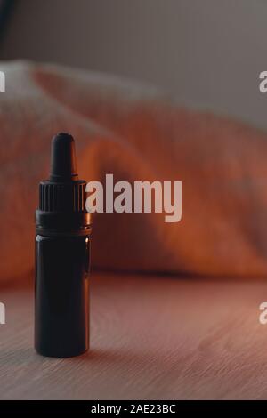 Singola 10 ml nero flacone di vetro bianco sul tavolo di legno Retroilluminato con luce rossa Foto Stock