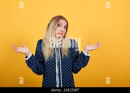 Deluso giovane donna cercando confuso, diffonde le mani sulla parete arancione Foto Stock