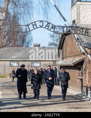 06 dicembre 2019, Polonia, Oswiecim: Cancelliere federale Angela Merkel (CDU) visite il tedesco ex campo di concentramento di Auschwitz e passeggiate sotto il cancello di ingresso con le parole "Arbeit macht frei" (Lavoro rende libero) insieme con il Primo Ministro polacco Mateusz Morawiecki (a destra di Merkel) e Piotr Cywinski (a sinistra di Merkel), Direttore del Memoriale di Auschwitz-Birkenau e Presidente della Fondazione di Auschwitz-Birkenau. Andrzej Kacorzyk, Vice Direttore del Museo di Auschwitz-Birkenau, va all'estrema destra. Merkel ha accettato un invito da parte della fondazione di Auschwitz-Birkenau, whi Foto Stock