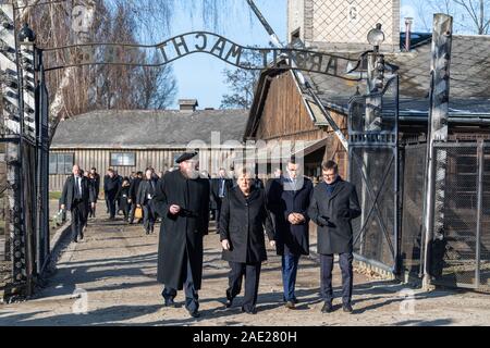 06 dicembre 2019, Polonia, Oswiecim: Cancelliere federale Angela Merkel (CDU) visite il tedesco ex campo di concentramento di Auschwitz e passeggiate sotto il cancello di ingresso con le parole "Arbeit macht frei" (Lavoro rende libero) insieme con il Primo Ministro polacco Mateusz Morawiecki (a destra di Merkel) e Piotr Cywinski (a sinistra di Merkel), Direttore del Memoriale di Auschwitz-Birkenau e Presidente della Fondazione di Auschwitz-Birkenau. Andrzej Kacorzyk, Vice Direttore del Museo di Auschwitz-Birkenau, va all'estrema destra. Merkel ha accettato un invito da parte della fondazione di Auschwitz-Birkenau, whi Foto Stock