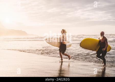 Montare felici amici divertendosi surf sul tramonto - Surfers padre e figlio in esecuzione fuori l'oceano - Sportivo lo stile di vita delle persone ed extreme sport concept Foto Stock