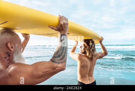 Montare felici amici divertendosi surf sul oceano tropicale - Surfers padre e figlio facendo stretching esercizi di surf Foto Stock