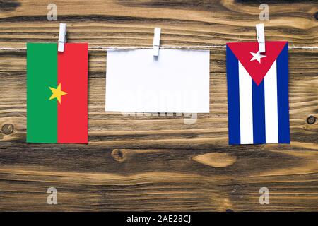 Appendere bandiere di Burkina Faso e Cuba attaccata alla corda con vestiti perni con copia spazio bianco sulla nota carta su sfondo di legno.Relazione Diplomatica Foto Stock
