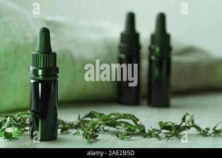 Composizione orizzontale di tre 10 ml nero bottiglie di vetro circondato da erbe essiccate su bianco tavolo in legno con retroilluminazione a freddo con luce verde Foto Stock