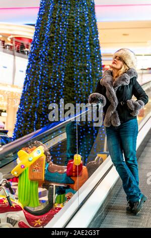 Donna attraente è scendendo le scale mobili in un grande magazzino mentre lei sta facendo shopping d'inverno Foto Stock